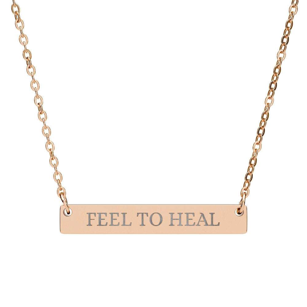 Rose gold bar necklace with engraved text "FEEL TO HEAL" on a sleek matte pendant, suspended on a delicate matching rose gold chain. Minimalist motivational affirmation jewelry for emotional healing and self-care.