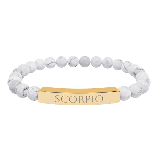 Bracelet with polished white howlite beads featuring natural gray-black veining and marbling, paired with a gold-plated curved bar engraved "SCORPIO" in uppercase letters. Stretch-fit zodiac-inspired crystal jewelry for intensity, transformation, and emotional depth.