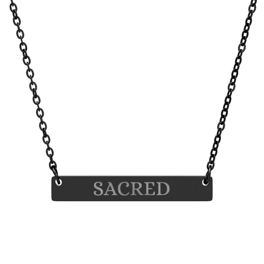 Black bar necklace with engraved uppercase text "SACRED" on a matte black pendant, suspended on a delicate black chain. Minimalist spiritual affirmation jewelry for sacred energy and divine connection.16.1sFast