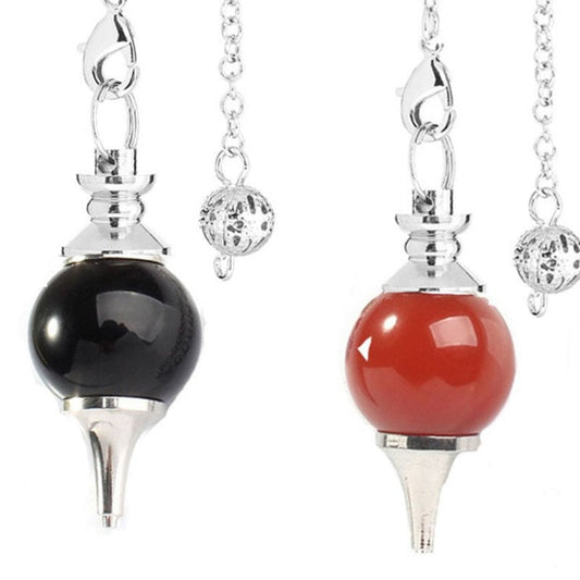 Two silver pendulums side by side: one with a glossy black onyx sphere and one with a glossy red carnelian sphere. Both have pointed metal tips and ornate silver chains with decorative acorn charms. Divination and dowsing tools.