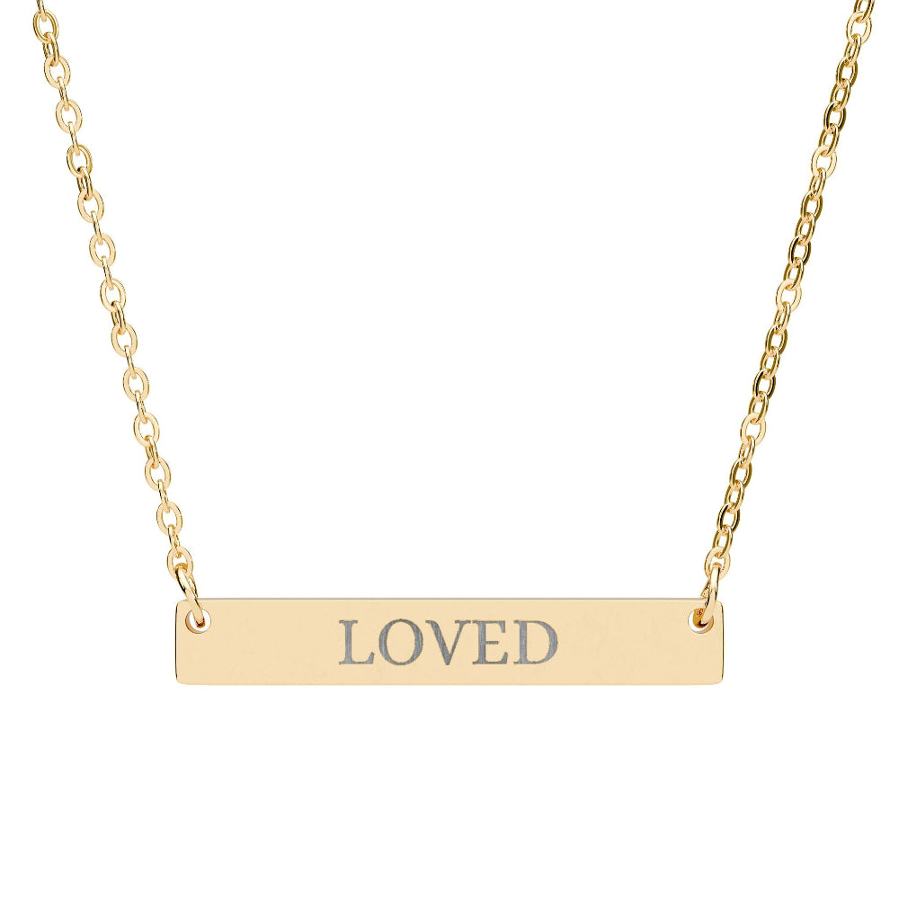 Gold bar necklace with engraved uppercase text "LOVED" on a sleek matte pendant, suspended on a delicate matching gold chain. Minimalist motivational affirmation jewelry for self-love, worthiness, and emotional healing.