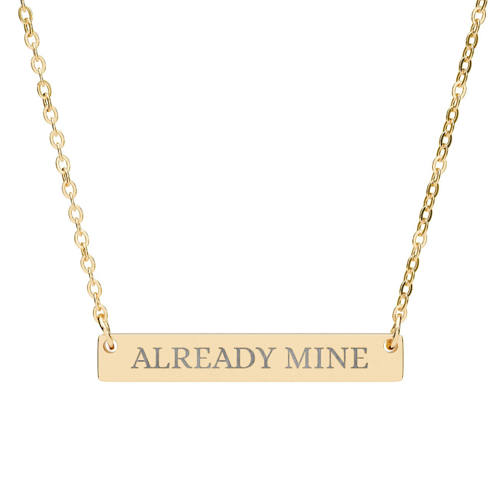 Gold bar necklace with engraved uppercase text "ALREADY MINE" on a sleek matte gold pendant, suspended on a delicate matching gold chain. Minimalist motivational affirmation jewelry for self-ownership, confidence, and empowerment.
