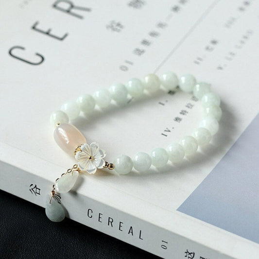 Light green jade beaded bracelet with translucent pinkish agate focal bead, gold plum blossom charm, and dangling jade-amethyst teardrop pendants on open book
