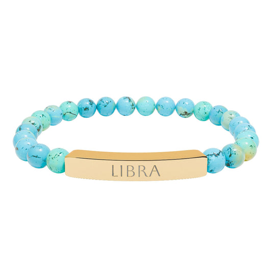 Bracelet with polished turquoise beads in soft aqua-blue tones with natural veining and speckles, featuring a gold-plated curved bar engraved "LIBRA" in uppercase letters. Stretch-fit zodiac-inspired crystal jewelry.