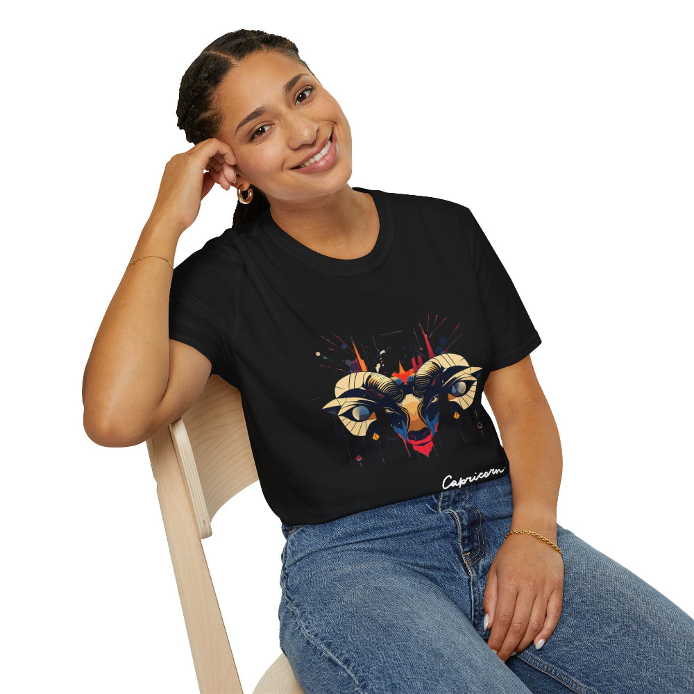 Black unisex cotton t-shirt modeled by smiling woman with braided hair, seated pose, hand on cheek, featuring bold Capricorn zodiac graphic: vibrant abstract goat/ram head portrait with large curved horns, intense expression, geometric diamond accents, flowing beard details, and dynamic multicolored paint splatters in gold, red, navy, teal, and black tones exploding outward. Elegant black cursive "Capricorn" text below. Astrology zodiac motivational crewneck tee.