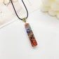 Rectangular orgonite pendant necklace in clear resin with embedded healing gemstones (turquoise, carnelian, amethyst, lapis) and copper spiral wire design, gold engraved triangular bail on black cord, spiritual energy jewelry on white background