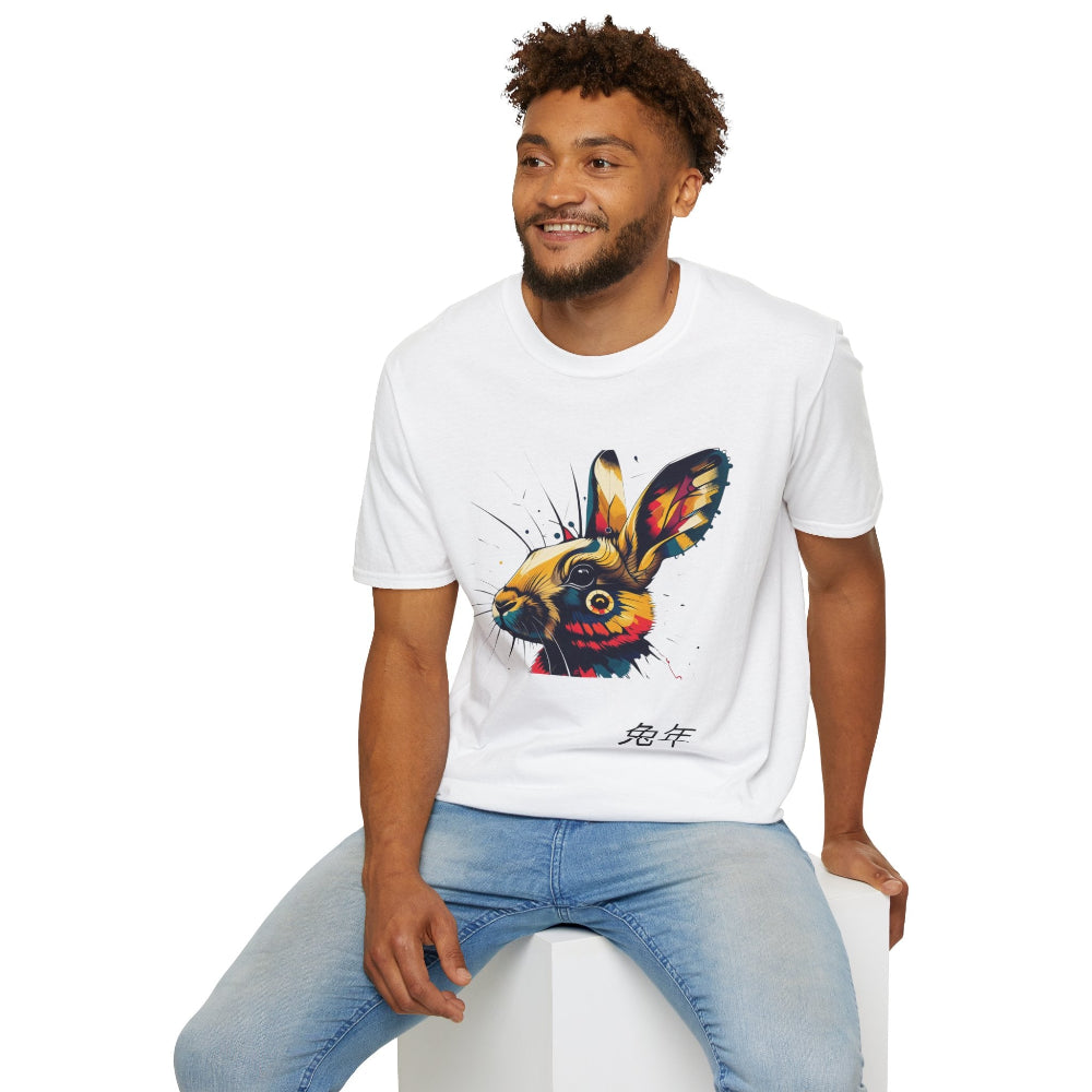 White unisex cotton t-shirt modeled by smiling man with curly hair and beard, featuring bold Year of the Rabbit graphic: vibrant abstract rabbit face portrait with large expressive ears, intense eyes, geometric patterns, and dynamic multicolored paint splatters in gold, red, blue, teal, orange, and black tones exploding outward. Chinese text "兔年" (Year of the Rabbit) printed below in black. Zodiac Chinese New Year motivational crewneck tee.
