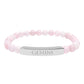 Bracelet with polished rose quartz beads in soft pink tones, natural translucent glow, paired with a silver curved bar engraved "GEMINI" in uppercase letters. Stretch-fit zodiac-inspired crystal jewelry.