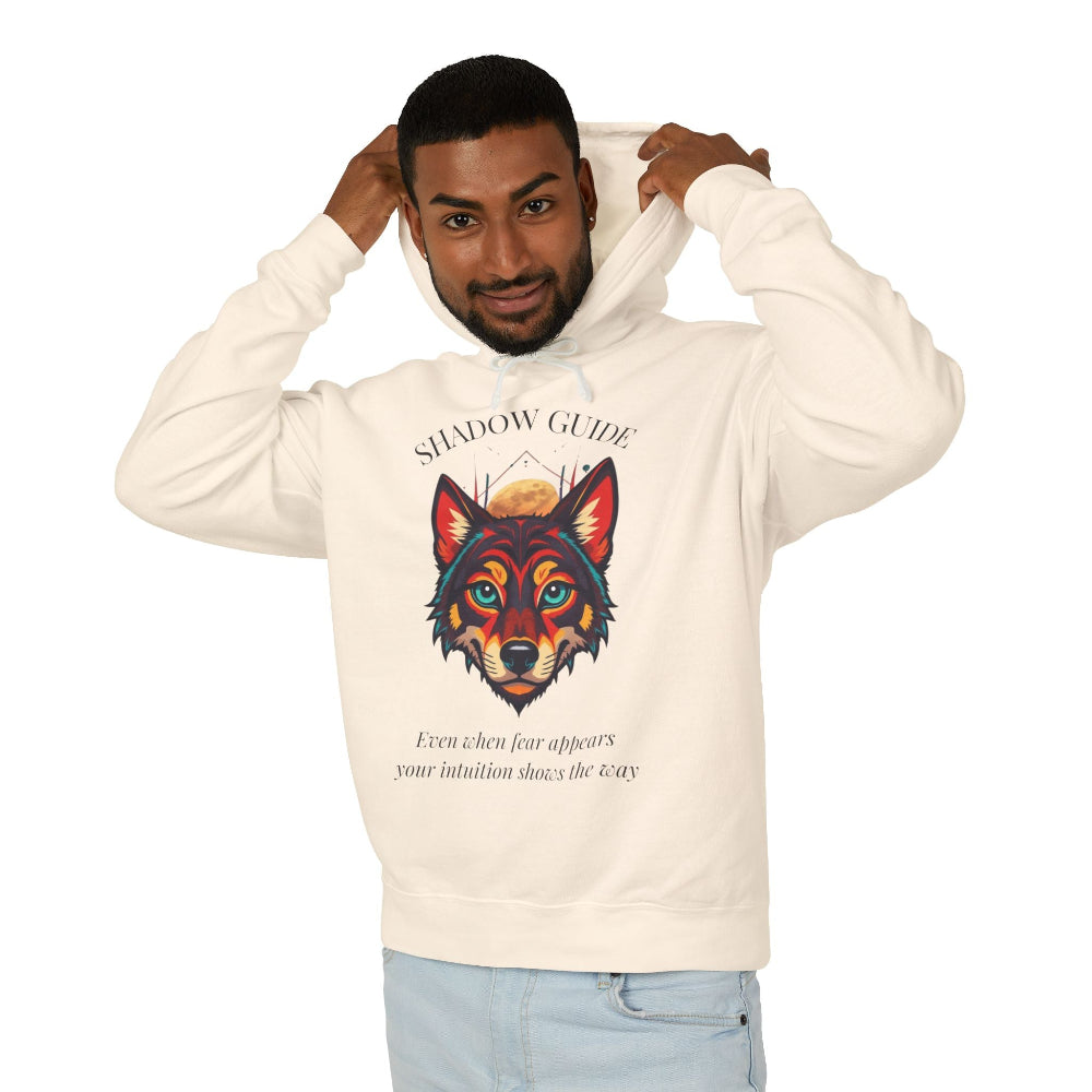 Young man with short hair pulling up the hood of a cream hoodie featuring vibrant multicolored wolf head graphic, intense eyes in orange blue teal splashes, full moon above, "SHADOW GUIDE" arched text, motivational quote about intuition and fear below