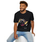 Black unisex cotton t-shirt modeled by smiling man with curly hair and beard, seated pose, featuring bold Year of the Horse graphic: vibrant abstract horse head portrait with detailed mane, intense eye, bridle and harness, geometric accents, and dynamic multicolored paint splatters in gold, blue, red, black, and teal tones exploding outward. Chinese text "马年" (Year of the Horse) printed below in white. Zodiac Chinese New Year motivational crewneck tee.