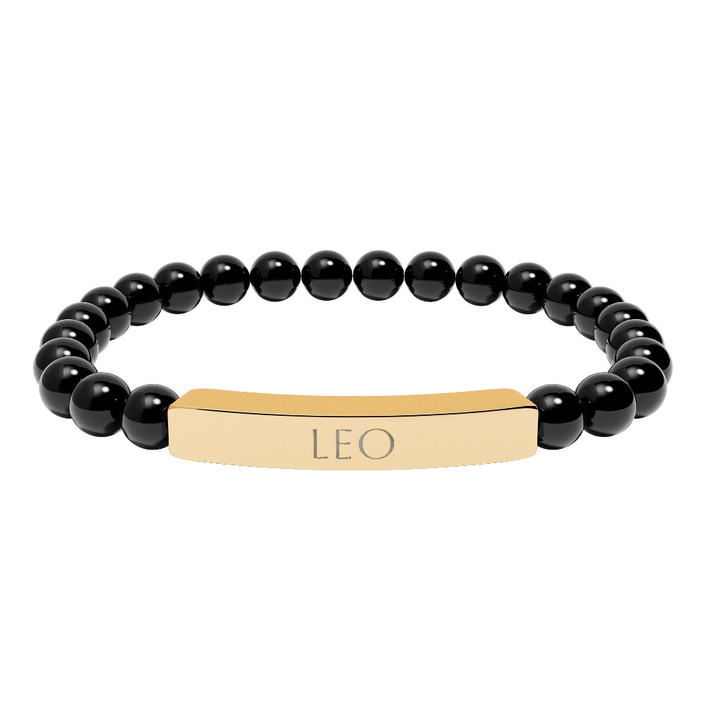 Bracelet with polished black onyx beads and gold-plated curved bar engraved "LEO" in uppercase letters. Stretch-fit zodiac-inspired crystal jewelry.