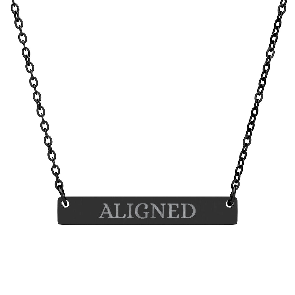 Black bar necklace with engraved uppercase text "ALIGNED" on a matte black pendant, suspended on a delicate black chain. Minimalist motivational affirmation jewelry for alignment, balance, and spiritual harmony.