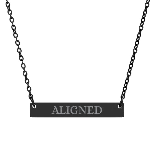 Black bar necklace with engraved uppercase text "ALIGNED" on a matte black pendant, suspended on a delicate black chain. Minimalist motivational affirmation jewelry for alignment, balance, and spiritual harmony.