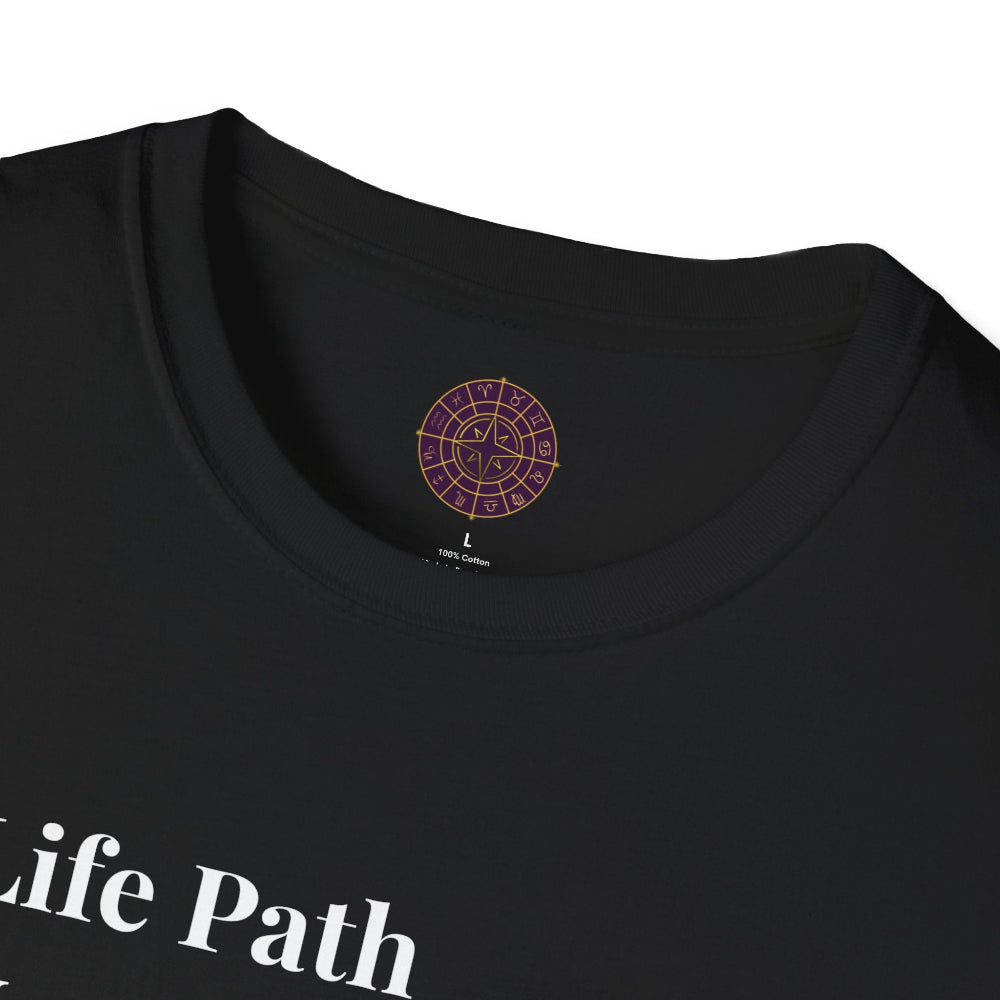 Black unisex cotton t-shirt neckline close-up detail: soft ribbed crewneck collar with clean stitching, comfortable fit, inner tag featuring a purple and gold circular zodiac wheel logo with 12 astrological signs arranged around the rim and central glowing star compass design. 100% cotton premium quality label visible. Essential motivational tee collar detail.