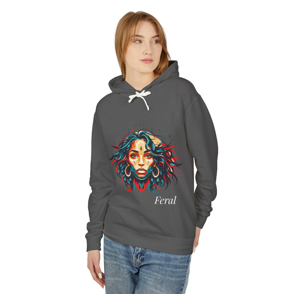 Young woman with long hair modeling charcoal gray hoodie featuring vibrant artistic portrait of a fierce woman with curly multicolored flowing hair, teal and red face accents, large hoop earrings, third-eye symbol, "Feral" text below