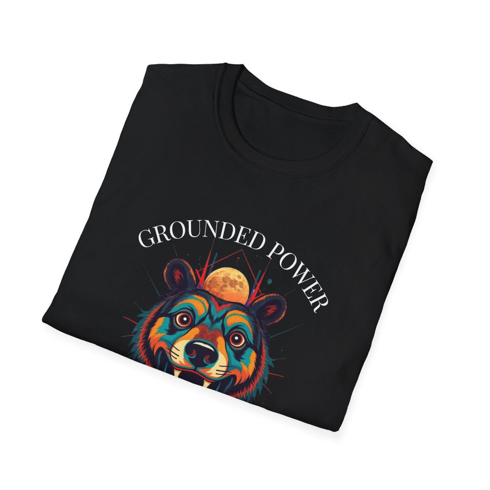Black folded unisex cotton t-shirt featuring bold "Grounded Power" graphic: vibrant abstract bear head portrait with intense expression, colorful geometric accents, and dynamic paint splatters in red, orange, teal, blue, and gold tones bursting outward around an orange moon background. Arched white text "GROUNDED POWER" above and smaller inspirational quote "Even when life is overwhelming, your roots keep you steady" below. Motivational spiritual empowerment crewneck tee.