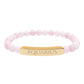 Bracelet with polished rose quartz beads in soft pink tones, natural translucent glow, paired with a gold-plated curved bar engraved "AQUARIUS" in uppercase letters. Stretch-fit zodiac-inspired crystal jewelry.