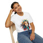 White unisex cotton t-shirt modeled by smiling woman with braided hair, hand on cheek, featuring bold "Feral" graphic on chest: vibrant abstract portrait of a fierce woman with wild flowing multicolored hair, intense expression, tribal markings, colorful geometric accents, and dynamic paint splatters in red, orange, teal, blue, and gold tones bursting outward around an orange moon background. White elegant cursive "Feral" text below. Wild feminine energy motivational crewneck tee.