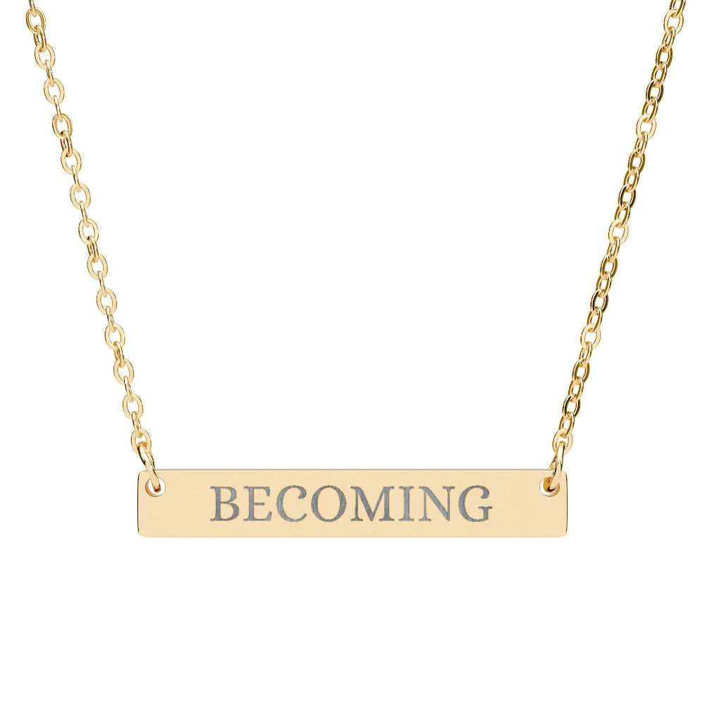 Gold bar necklace featuring engraved uppercase text "BECOMING" on a sleek matte pendant, suspended on a delicate matching gold chain. Minimalist motivational affirmation jewelry for growth, transformation, and self-evolution.