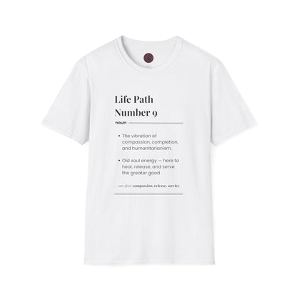 White unisex cotton t-shirt laid out flat featuring bold Life Path Number 9 numerology print in dictionary style: exact text reading "Life Path Number 9 noun · The vibration of compassion, completion, and humanitarianism. · Old soul energy — here to heal, release, and serve the greater good. – see also: compassion, release, service". Motivational spiritual numerology crewneck tee flat lay with visible purple/gold zodiac wheel inner tag.