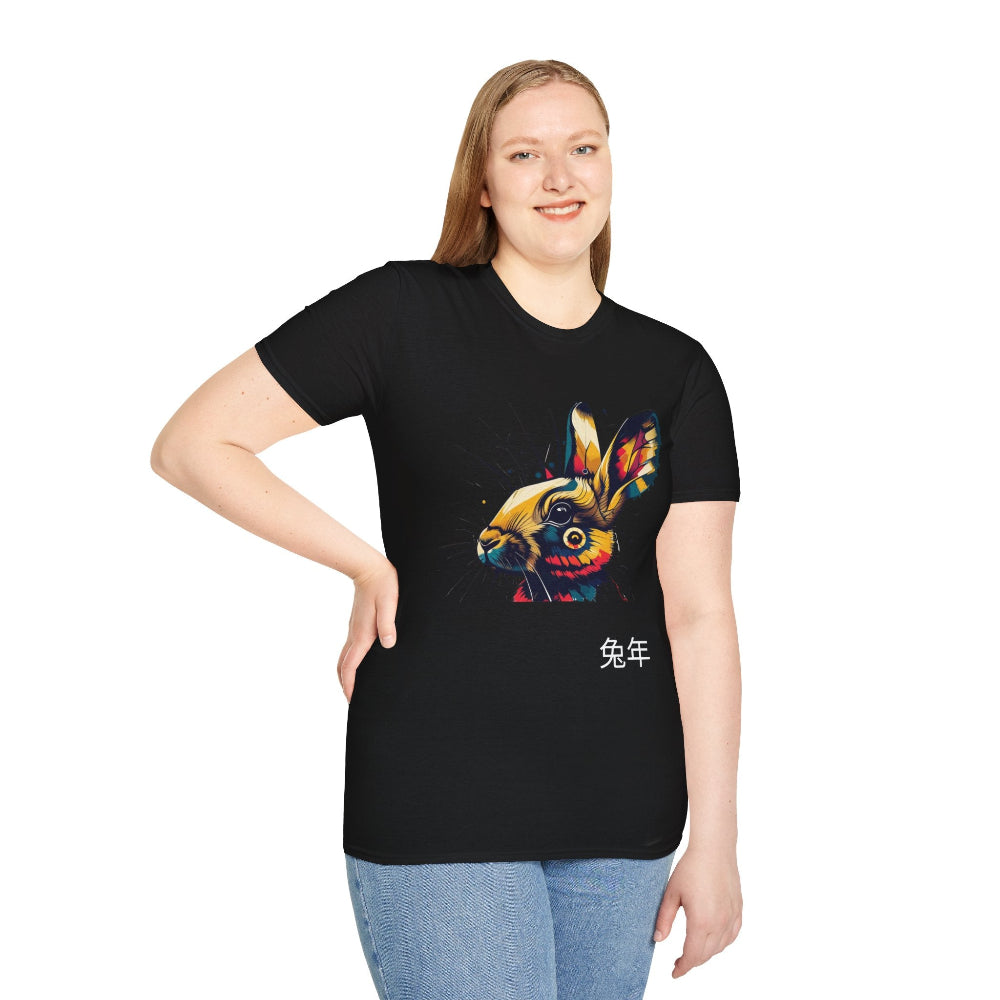 Black unisex cotton t-shirt modeled by smiling plus-size female with long blonde hair, hand on hip, featuring bold Year of the Rabbit graphic: vibrant abstract rabbit face portrait with large expressive ears, intense glowing eyes, geometric patterns, and dynamic multicolored paint splatters in gold, red, blue, teal, orange, and black tones exploding outward. Chinese text "兔年" (Year of the Rabbit) printed below in white. Zodiac Chinese New Year motivational crewneck tee.