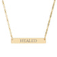 Gold bar necklace with engraved uppercase text "HEALED" on a sleek matte pendant, suspended on a delicate matching gold chain. Minimalist motivational affirmation jewelry for healing, recovery, and emotional restoration.