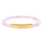 Bracelet with polished rose quartz beads in soft pink tones, natural translucent glow, paired with a gold-plated curved bar engraved "ARIES" in uppercase letters. Stretch-fit zodiac-inspired crystal jewelry for passion, courage, and leadership.