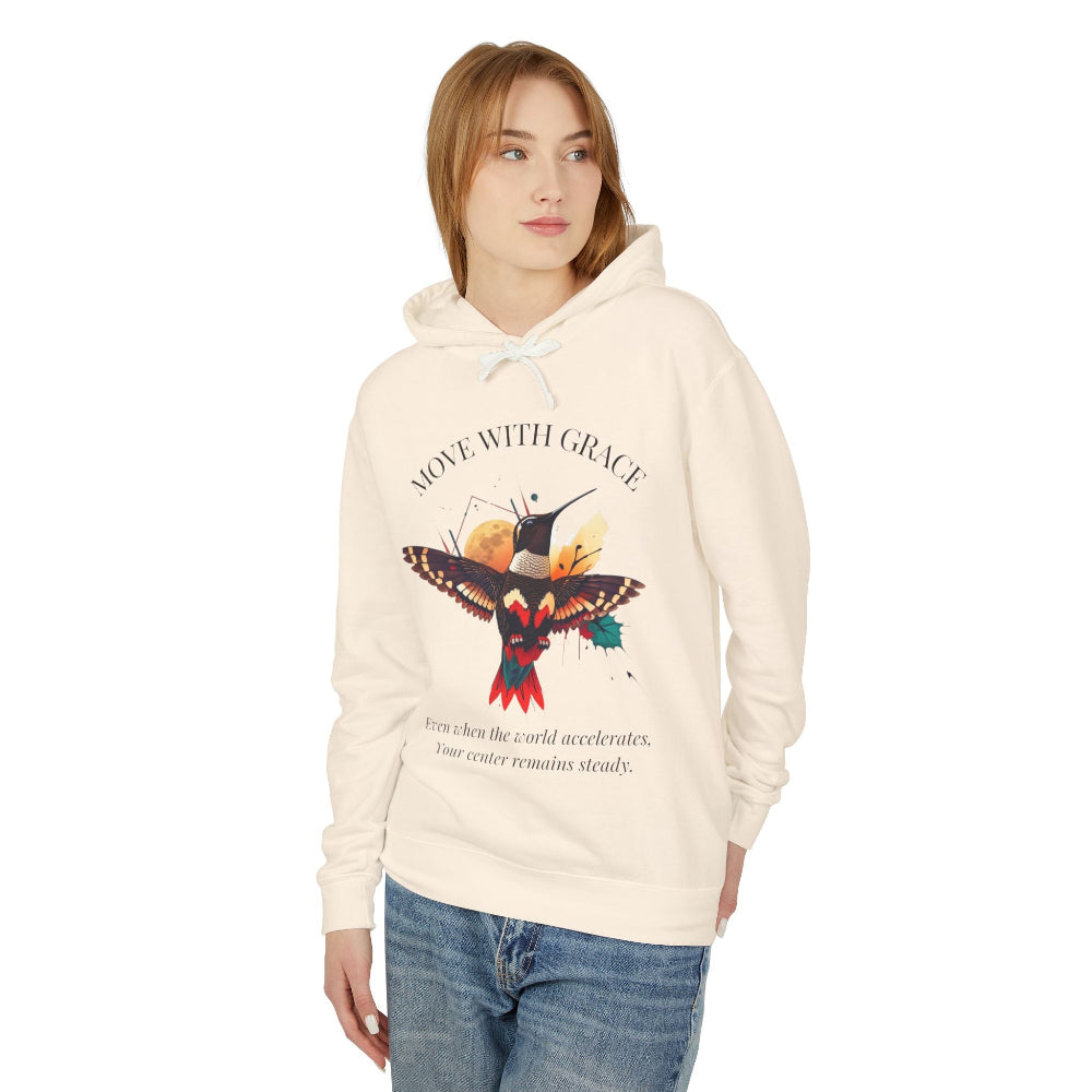 Women's cream-colored "Move With Grace" hummingbird graphic hoodie. Features a vibrant nature-inspired illustration and inspirational quote in black text.