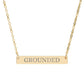 Gold bar necklace with engraved uppercase text "GROUNDED" on a sleek matte pendant, suspended on a delicate matching gold chain. Minimalist motivational affirmation jewelry for grounding, stability, and root chakra energy.