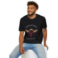 Black unisex cotton t-shirt modeled by smiling man with curly hair and beard, featuring bold "Sacred Alignment" graphic on chest: vibrant abstract bee with detailed wings and body, colorful geometric accents, and dynamic paint splatters in red, orange, teal, blue, and gold tones around an orange moon. Arched white text "SACRED ALIGNMENT" above and smaller quote "Even when progress is quiet, the universe is conspiring" below. Motivational spiritual empowerment crewneck tee.