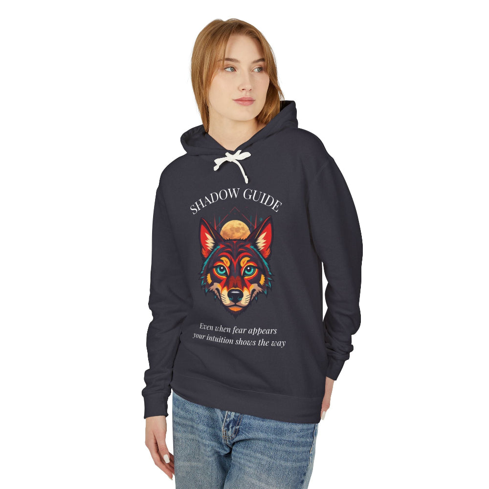 Young woman with long hair modeling charcoal gray hoodie featuring vibrant multicolored wolf head graphic, intense eyes in orange blue teal splashes, full moon above, "SHADOW GUIDE" arched text, motivational quote about intuition and fear below