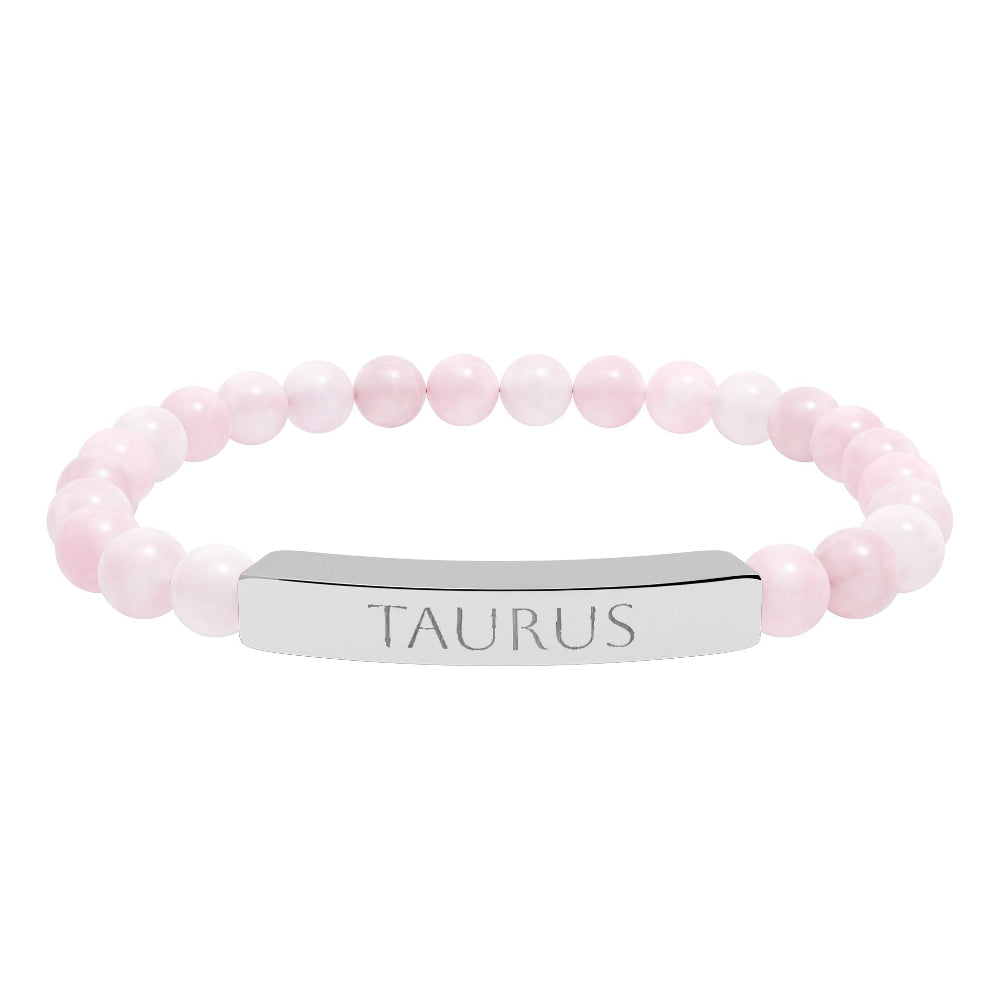 Bracelet with polished rose quartz beads in soft pink tones, natural translucent glow, paired with a silver curved bar engraved "TAURUS" in uppercase letters. Stretch-fit zodiac-inspired crystal jewelry.
