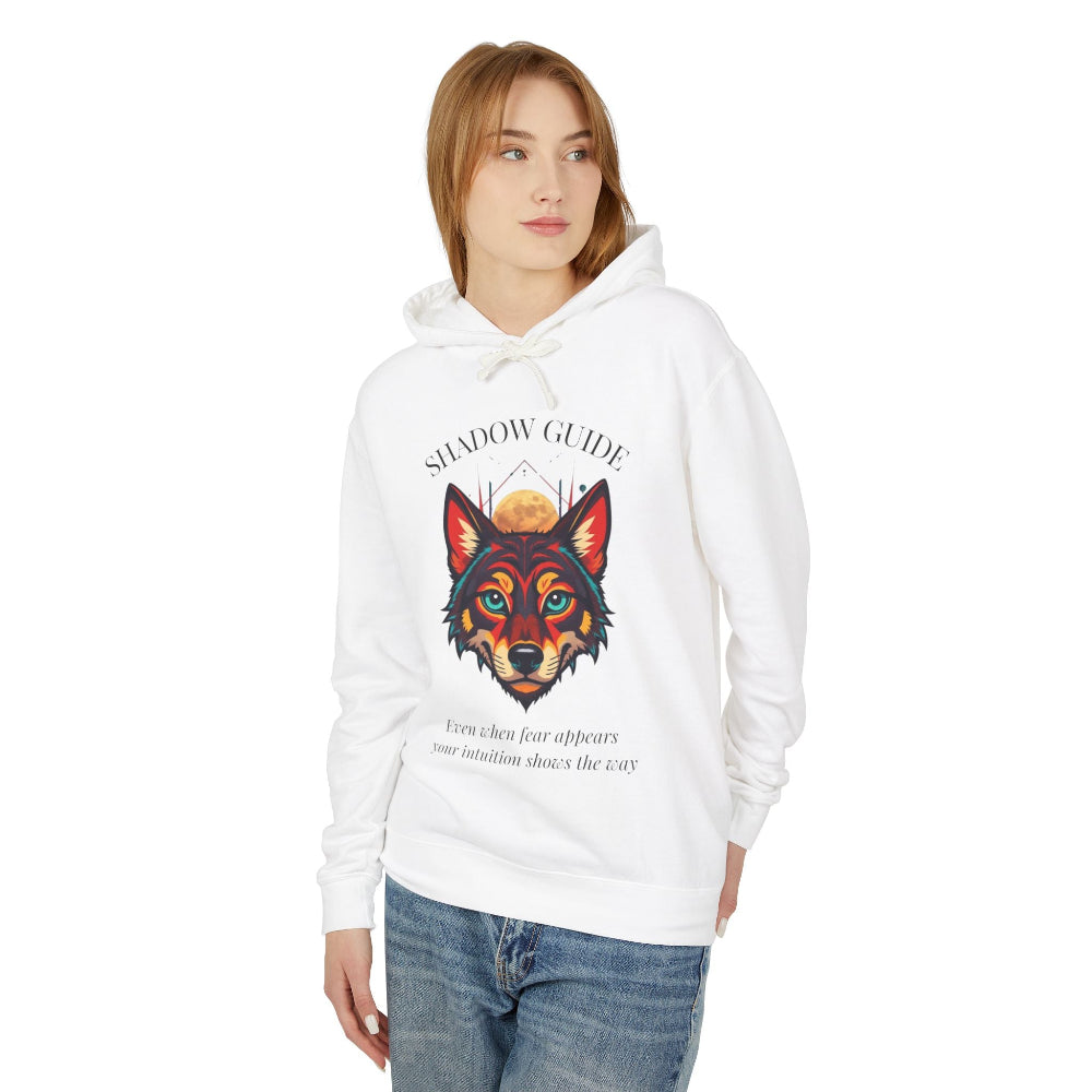 Young woman with long hair modeling white hoodie featuring vibrant multicolored wolf head graphic, intense eyes in orange blue teal splashes, full moon above, "SHADOW GUIDE" arched text, motivational quote about intuition and fear below