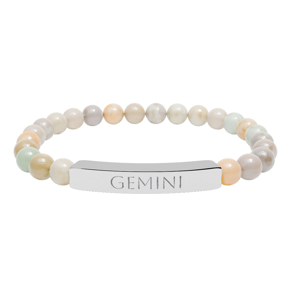 Bracelet with polished pastel beads in soft peach, cream, gray, and light blue tones with natural marbling, featuring a silver curved bar engraved "GEMINI" in uppercase letters. Stretch-fit zodiac-inspired crystal jewelry.