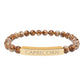 Bracelet with polished brown leopard jasper beads and gold-plated curved bar engraved "CAPRICORN" in uppercase letters. Stretch-fit zodiac-inspired natural stone jewelry for ambition, discipline, and grounding.