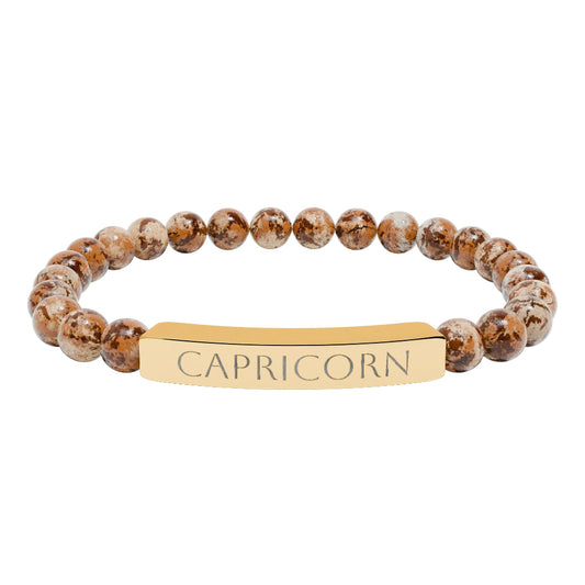 Bracelet with polished brown leopard jasper beads and gold-plated curved bar engraved "CAPRICORN" in uppercase letters. Stretch-fit zodiac-inspired natural stone jewelry for ambition, discipline, and grounding.