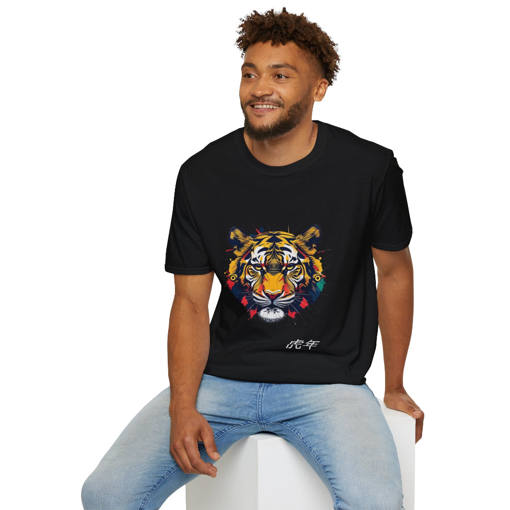 Black unisex cotton t-shirt modeled by smiling man with curly hair and beard, featuring bold Year of the Tiger graphic: vibrant abstract tiger face portrait with fierce intense eyes, detailed stripes, large ears, and dynamic multicolored paint splatters in yellow, orange, red, blue, black, and teal tones exploding outward. Chinese text "虎年" (Year of the Tiger) printed below in white. Zodiac Chinese New Year motivational crewneck tee.