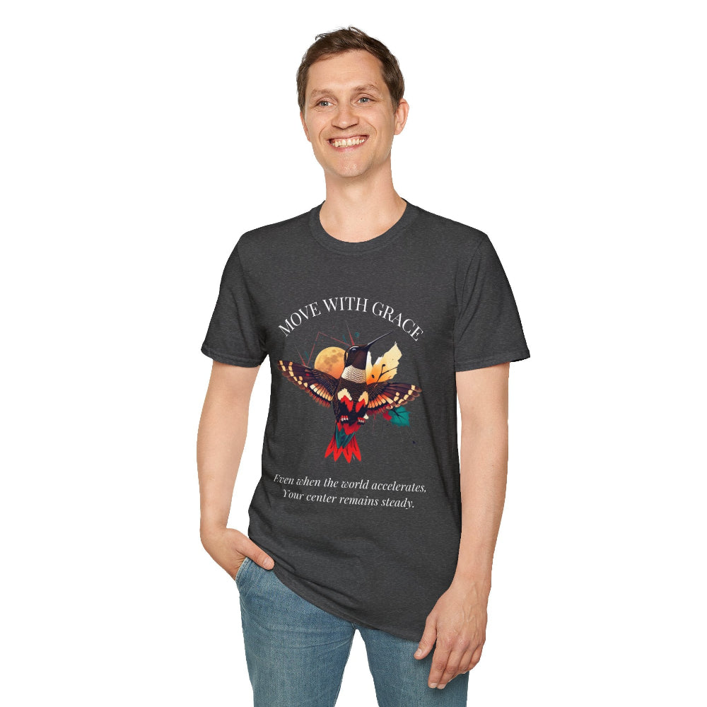 Man wearing a dark grey speckled t-shirt featuring a vibrant hummingbird graphic with the text "MOVE WITH GRACE" above and the quote "Even when the world accelerates, Your center remains steady" below. Casual motivational streetwear style with blue jeans.