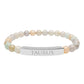 Bracelet with polished pastel beads in soft peach, cream, gray, and light blue tones with natural marbling, featuring a silver curved bar engraved "TAURUS" in uppercase letters. Stretch-fit zodiac-inspired crystal jewelry.