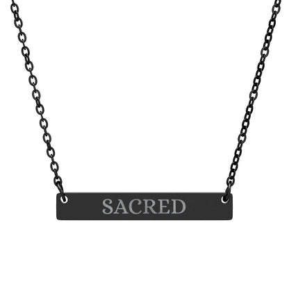 Black bar necklace with engraved uppercase text "SACRED" on a matte black pendant, suspended on a delicate black chain. Minimalist spiritual affirmation jewelry for sacred energy and divine connection.16.1sFast