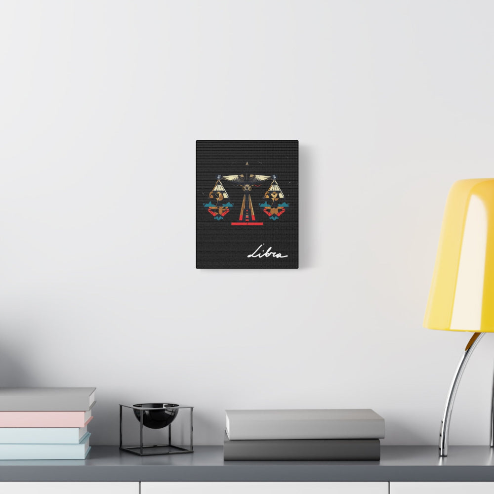 Black canvas wall art print of geometric Libra scales with intricate patterns and colorful accents on dark background, featuring "Libra" in elegant white cursive, displayed in a modern home décor setting above a console table with books and yellow lamp.