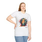 White plus-size unisex cotton t-shirt modeled by smiling woman with long blonde hair, hand on hip, featuring bold "Feral" graphic on chest: vibrant abstract portrait of a fierce woman with wild flowing multicolored hair, intense expression, tribal markings, colorful geometric accents, and dynamic paint splatters in red, orange, teal, blue, and gold tones bursting outward. White elegant cursive "Feral" text below. Wild feminine energy motivational crewneck tee.