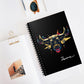 Black spiral-bound notebook with a bold Taurus zodiac bull illustration in gold, red, and blue on the cover, featuring stylized horns and artistic splashes, with “Taurus” written in white script at the bottom, placed on a clean desk with sunglasses and stationery items.