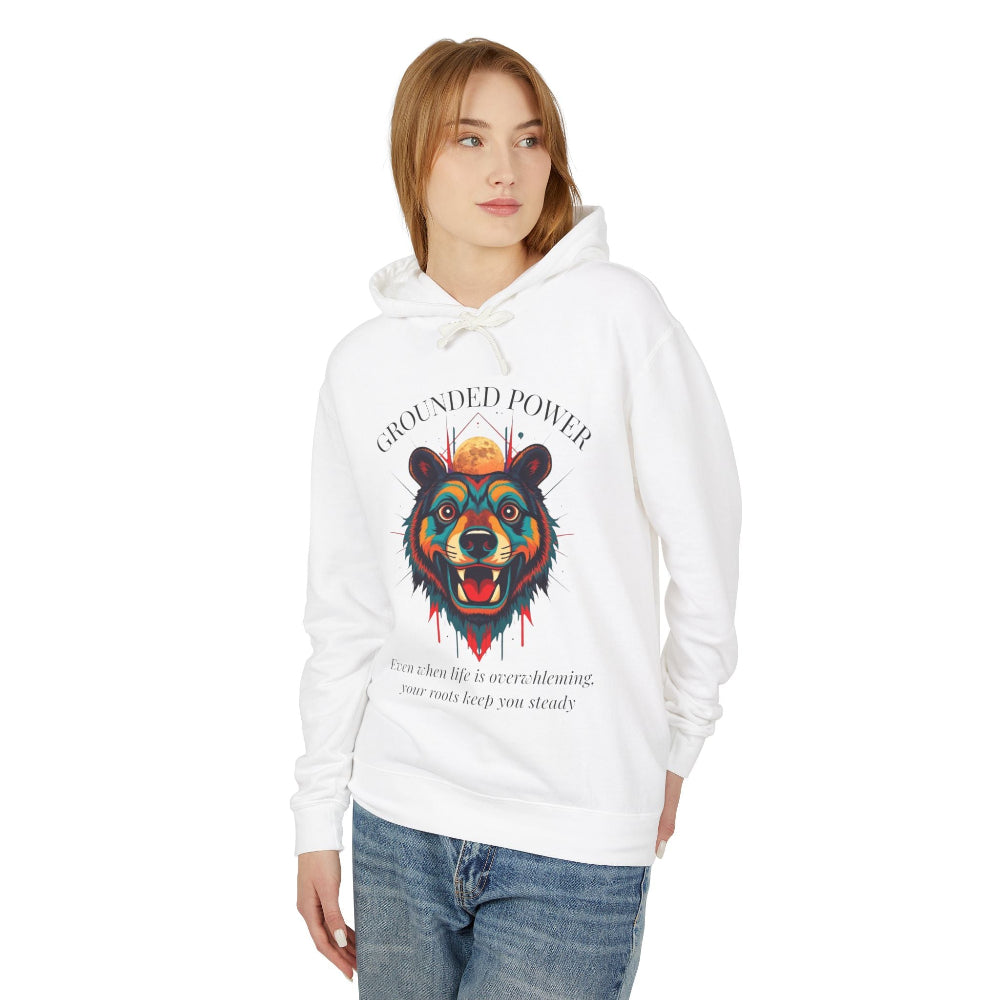 Young woman with long hair modeling white hoodie featuring vibrant multicolored bear head graphic, roaring expression, fur in blue orange teal splashes, orange moon above, "GROUNDED POWER" arched text, motivational quote about roots and steadiness below