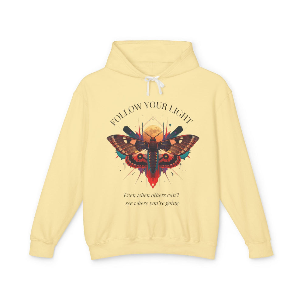 Light yellow hoodie with vibrant multicolored moth/butterfly graphic, geometric sun/moon elements, "FOLLOW YOUR LIGHT" arched text above, motivational quote "Even when others can't see where you're going" below