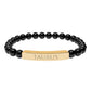 Bracelet with polished black onyx beads and gold-plated curved bar engraved "TAURUS" in uppercase letters. Stretch-fit zodiac-inspired crystal jewelry.