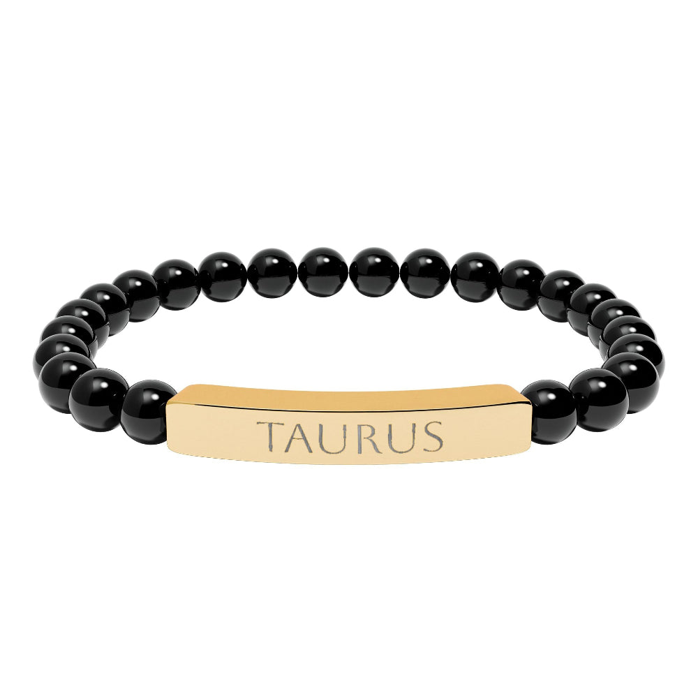 Bracelet with polished black onyx beads and gold-plated curved bar engraved "TAURUS" in uppercase letters. Stretch-fit zodiac-inspired crystal jewelry.