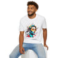White unisex cotton t-shirt modeled by smiling man with curly hair and beard, featuring bold "Primal" graphic: stylized bearded man portrait with colorful red, yellow, teal, and black paint splatters bursting outward. Elegant black cursive "Primal" text below. Primal masculine energy motivational crewneck tee.