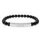 Bracelet with polished black onyx beads and silver curved bar engraved "LIBRA" in uppercase letters. Stretch-fit zodiac-inspired crystal jewelry.