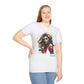 White plus-size unisex cotton t-shirt modeled by smiling woman with long blonde hair, hand on hip, featuring bold "Feral" graphic on chest: vibrant abstract portrait of a fierce woman with wild flowing hair, intense expression, tribal markings, colorful geometric accents, and dynamic paint splatters in red, orange, teal, blue, and gold tones bursting outward around an orange moon background. White elegant cursive "Feral" text below. Wild feminine energy motivational crewneck tee.